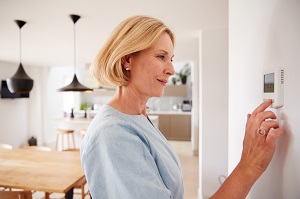 Woman Adjusting Central Heating Temperature At Home On Thermostat | energy-saving tips for hoa