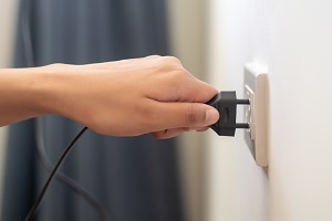 hand unplugging electrical wall outlet | save energy during summer