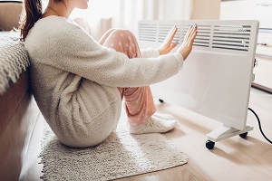 woman warming her hands on heater | prevent pipes from freezing