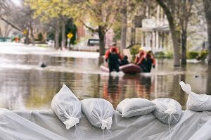 Flood Protection Sandbags with flooded homes in the background | what does hoa insurance cover