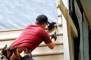 man wearing a tool belt fixing exterior of house | hoa exterior maintenance