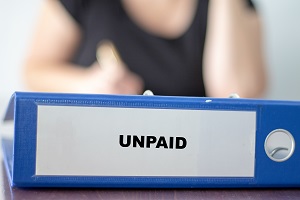 Folder labelled with the word unpaid in front of a woman sitting behind her office desk | hoa fees after death
