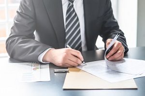 man signing document on office desk | D & O insurance for HOA