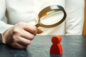 person examines a red man's figure through a magnifying glass | resident agent