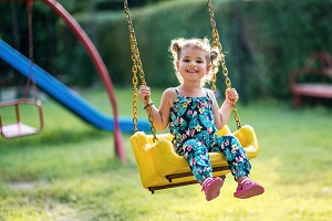 Happy little girl on a swing in the park | hoa playground equipment