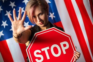 Woman with a STOP sign holds a forbidding sign with her hand with a background of the American flag | freedom to display the american flag act of 2005
