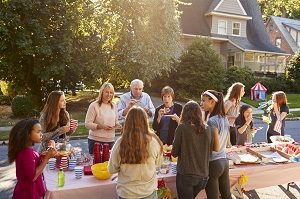 Neighbors talk and eat around a table at a block party | hoa natural disaster preparation
