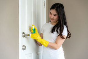 Woman spraying disinfectant to the door knob | hoa board members and coronavirus